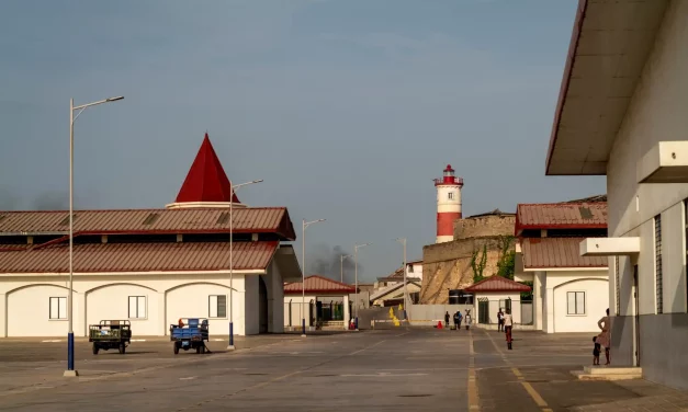Le nouveau port de p&ecirc;che inaugur&eacute; en septembre 2024, avec le phare colonial de 1932 en arri&egrave;re-plan. La tour de 28 m&egrave;tres, b&acirc;tie par l'administration britannique pour guider les navires vers le port d'Accra, doit son nom &agrave; James II, duc d'York. La fum&eacute;e provient des fours &agrave; poisson du quartier.
